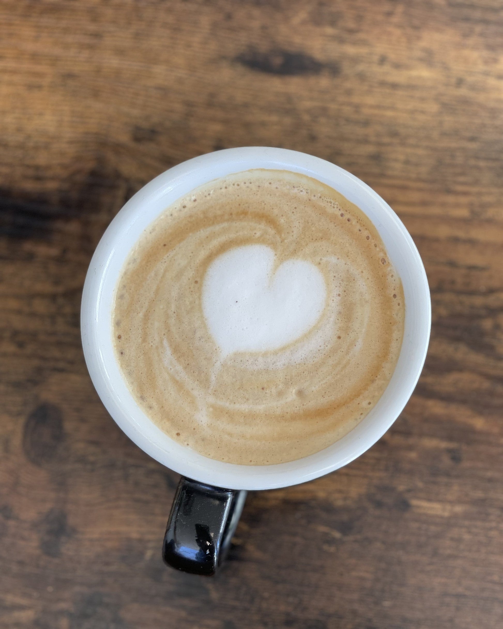 overhead view of a white cup of espresso with milk on a dark wood table